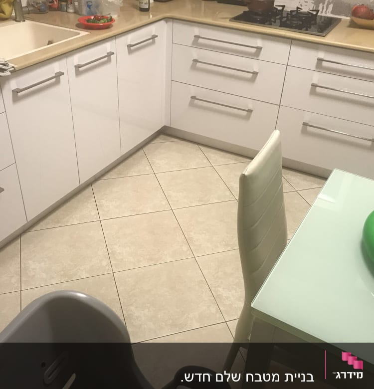 מטבח עם ארונות לבנים, כיור ושולחן זכוכית